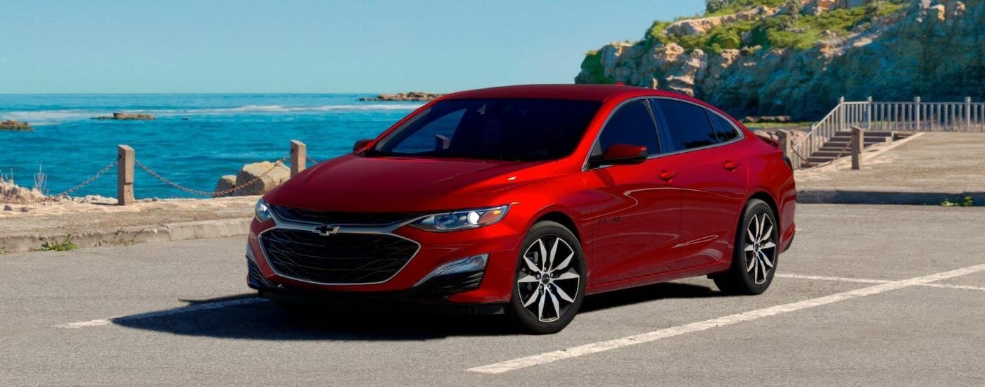 Car Dealership - 2024 Chevy Malibu - Ocean.jpg A red 2024 Chevy Malibu is show parked on a lot near the ocean.