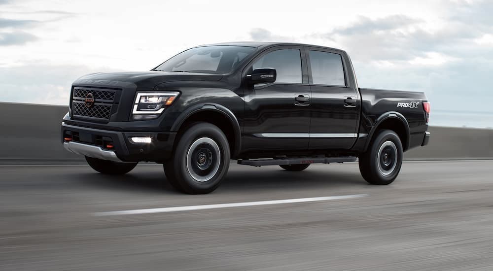 A black 2023 Nissan Titan PRO-4X is shown driving to view used cars for sale in Charlotte.