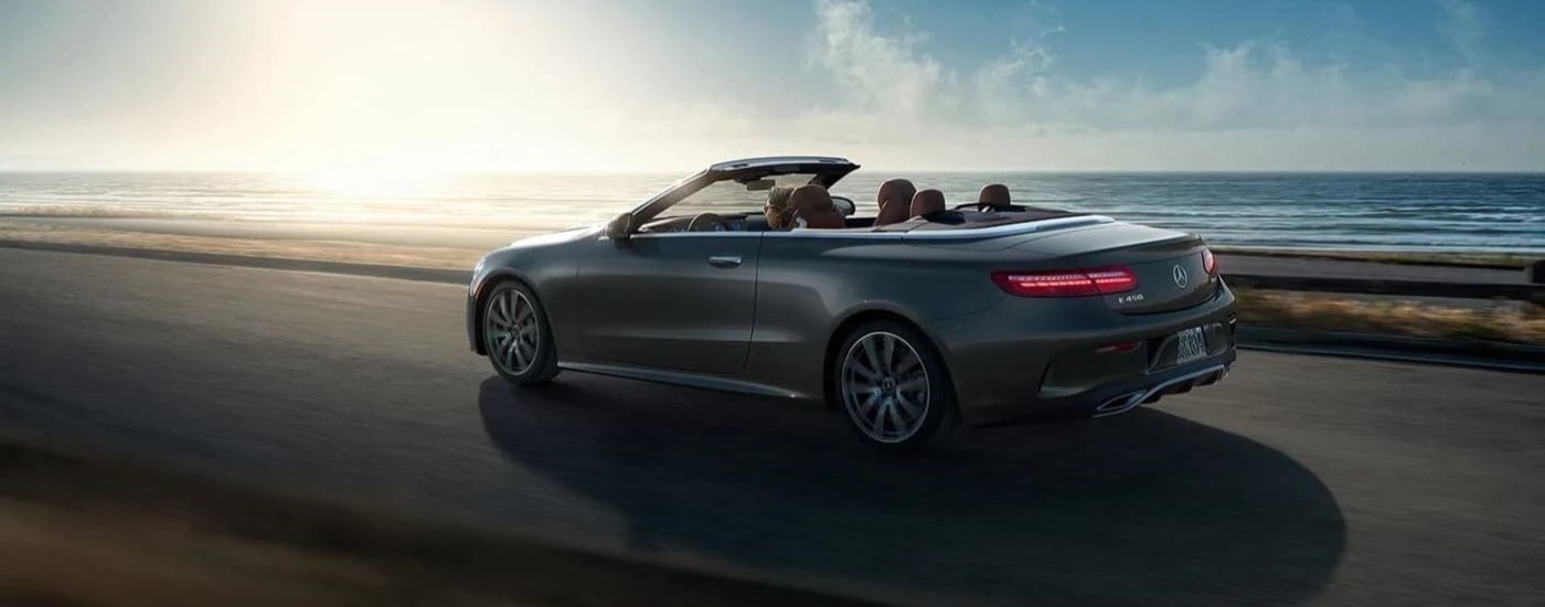 Car Dealership - 2022 Mercedes E-Class Cabriolet - Ocean.jpg A grey 2022 Mercedes E-Class Cabriolet is shown from the side driving past the ocean.