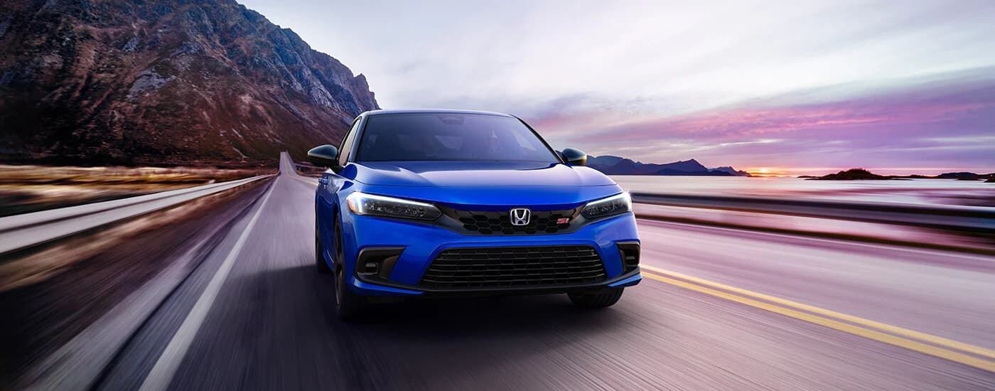 Car Dealership - 2023 Honda Civic Si - Sunrise.jpg A blue 2023 Honda Civic Si is shown on a coastal road at sunrise.