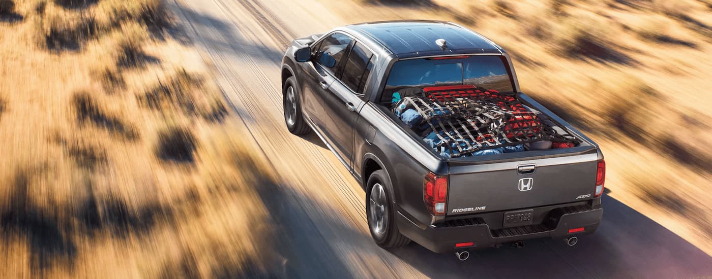 Truck%20Dealership%20Near%20Raleigh%20-%202022%20Honda%20Ridgeline%20-%20Grey%20Cargo.jpg A grey 2022 Honda Ridgeline is driving on a dusty dirt road with cargo in the bed.