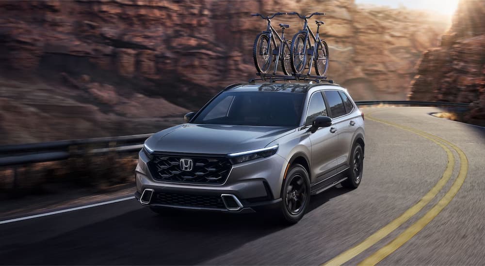 Grey 2025 Honda CR-V Sport Touring Hybrid driving around a bend.
