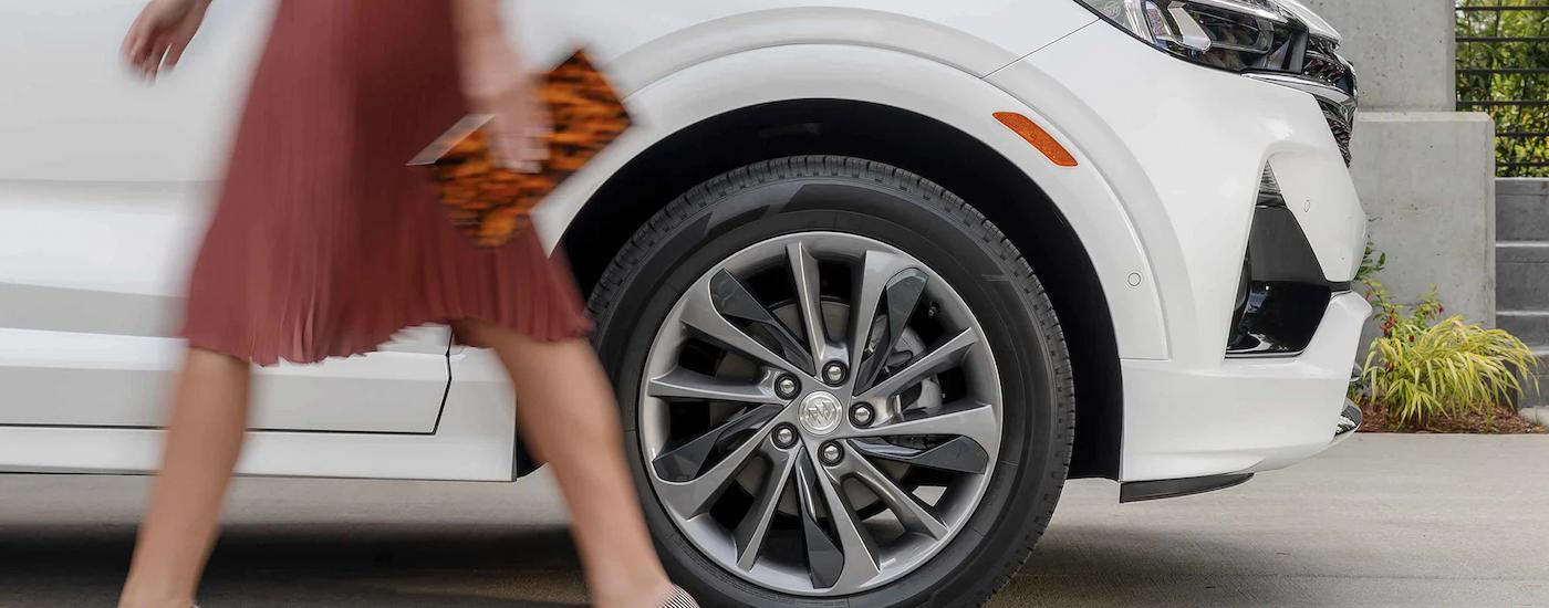 A person is shown walking past the front of a white 2022 Buick Encore GX Sport.