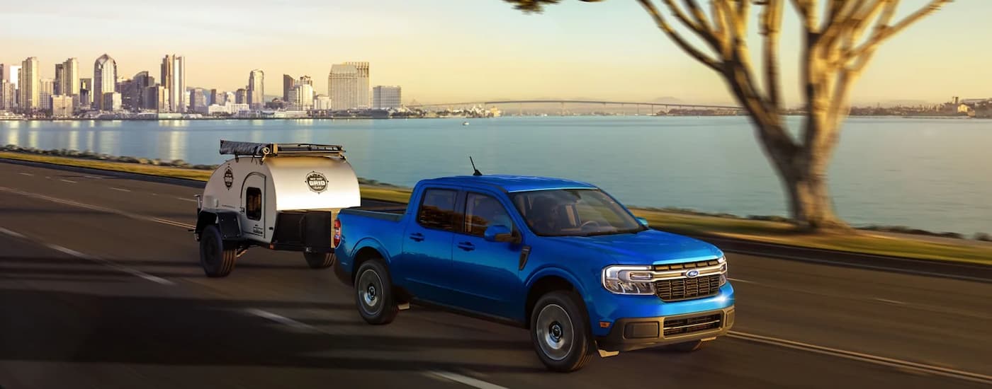 Truck%20Dealership%20Near%20Raleigh%20-%202023%20Ford%20Maverick%20-%20Towing.jpg A blue 2023 Ford Maverick is towing a small camper trailer after leaving a truck dealership near Raleigh.