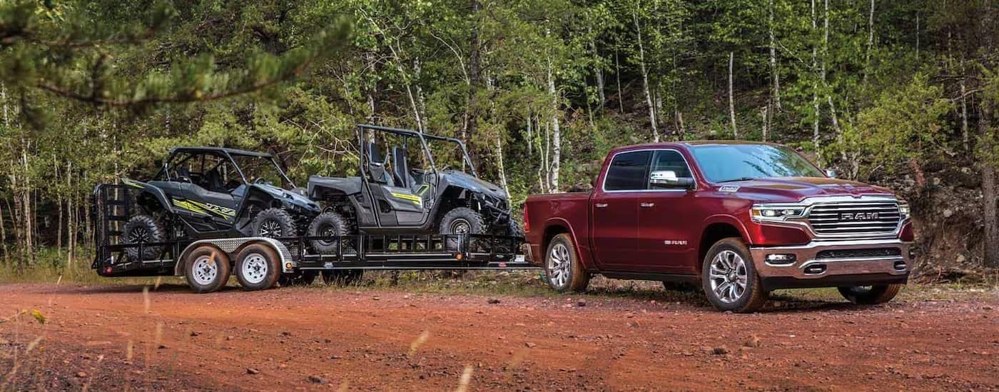 A red 2023 Ram 1500 towing a trailer off-road.