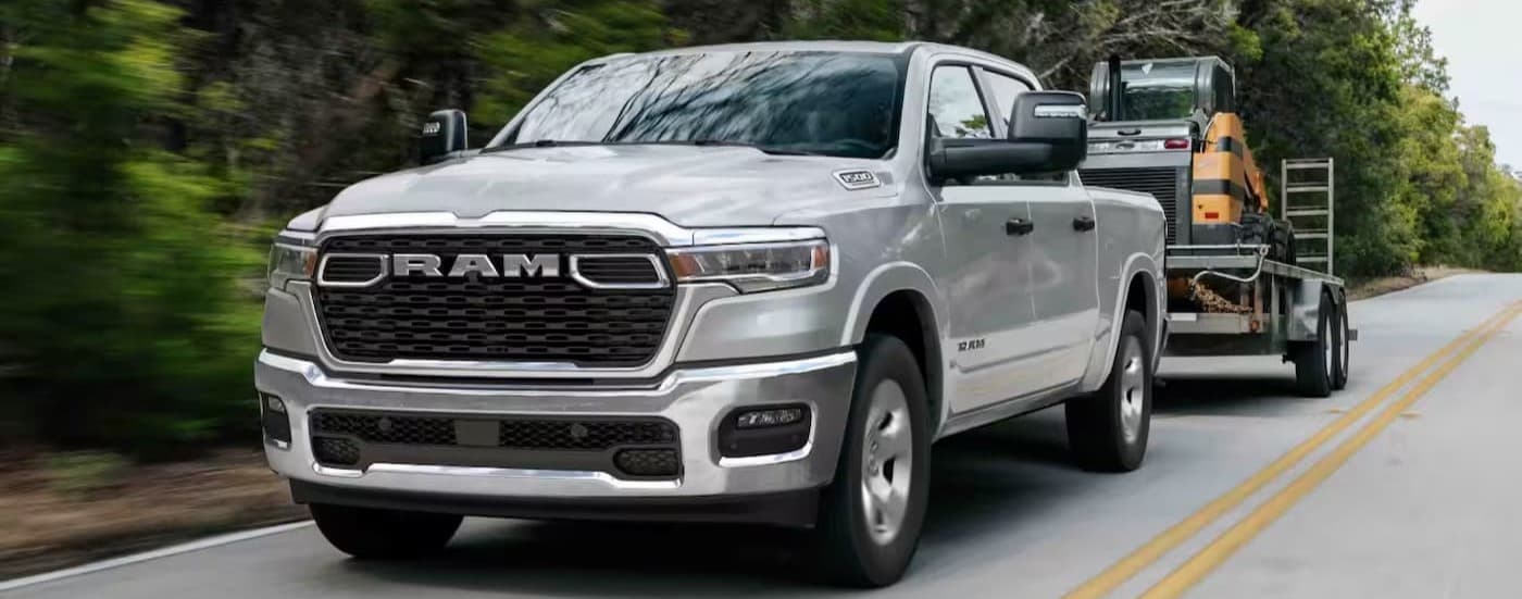 A silver 2026 Ram 1500 Big Horn towing a trailer on a highway.